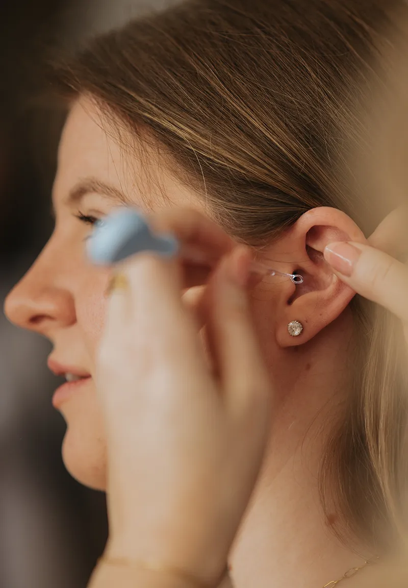 Modern office corner with a black mesh chair, wooden desk holding a computer screen displaying 'Ears4U Hearing Services', wall-mounted shelves with medical supplies, and two framed city skyline artworks.