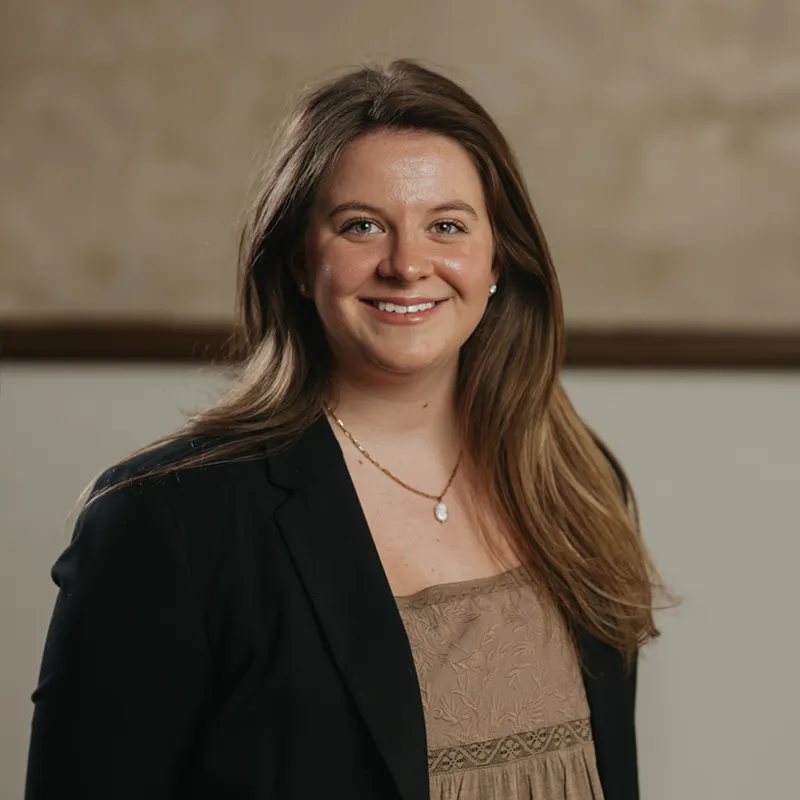 Woman with long black hair wearing glasses and a black outfit standing indoors near a white door, smiling.