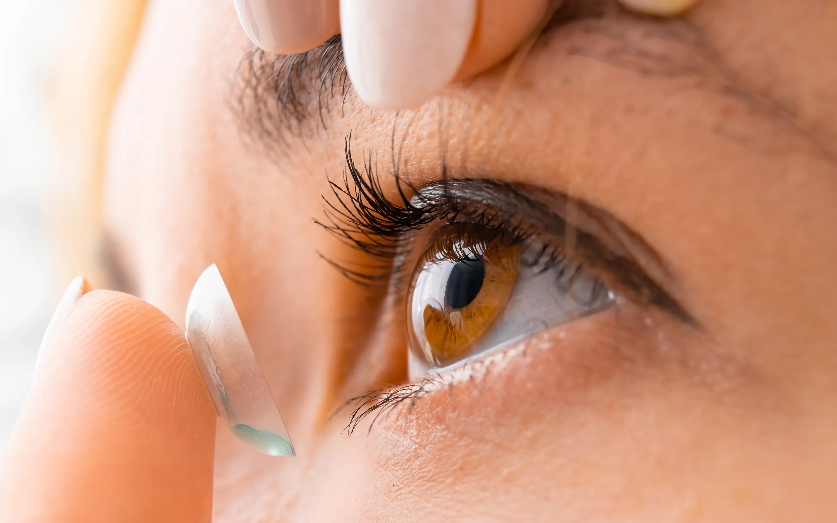 Contact lens insertion on brown eye demonstrating safe contact lens wear and care practices