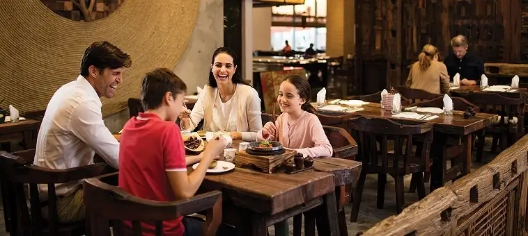 Family of four enjoying a meal and laughing together in a rustic-style restaurant.