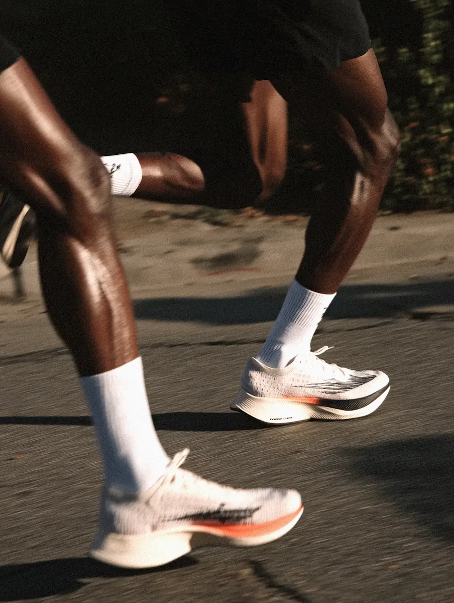 Close-up of two runners' legs in white running shoes and socks on a paved road.