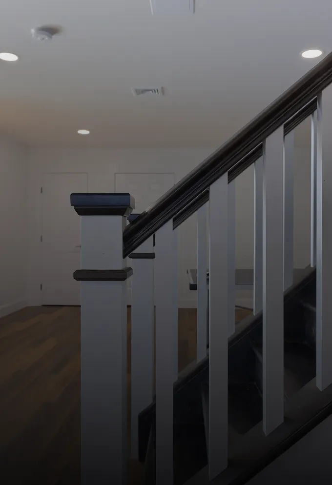 Close-up of a black and white staircase railing inside a modern home with wooden flooring and white walls.