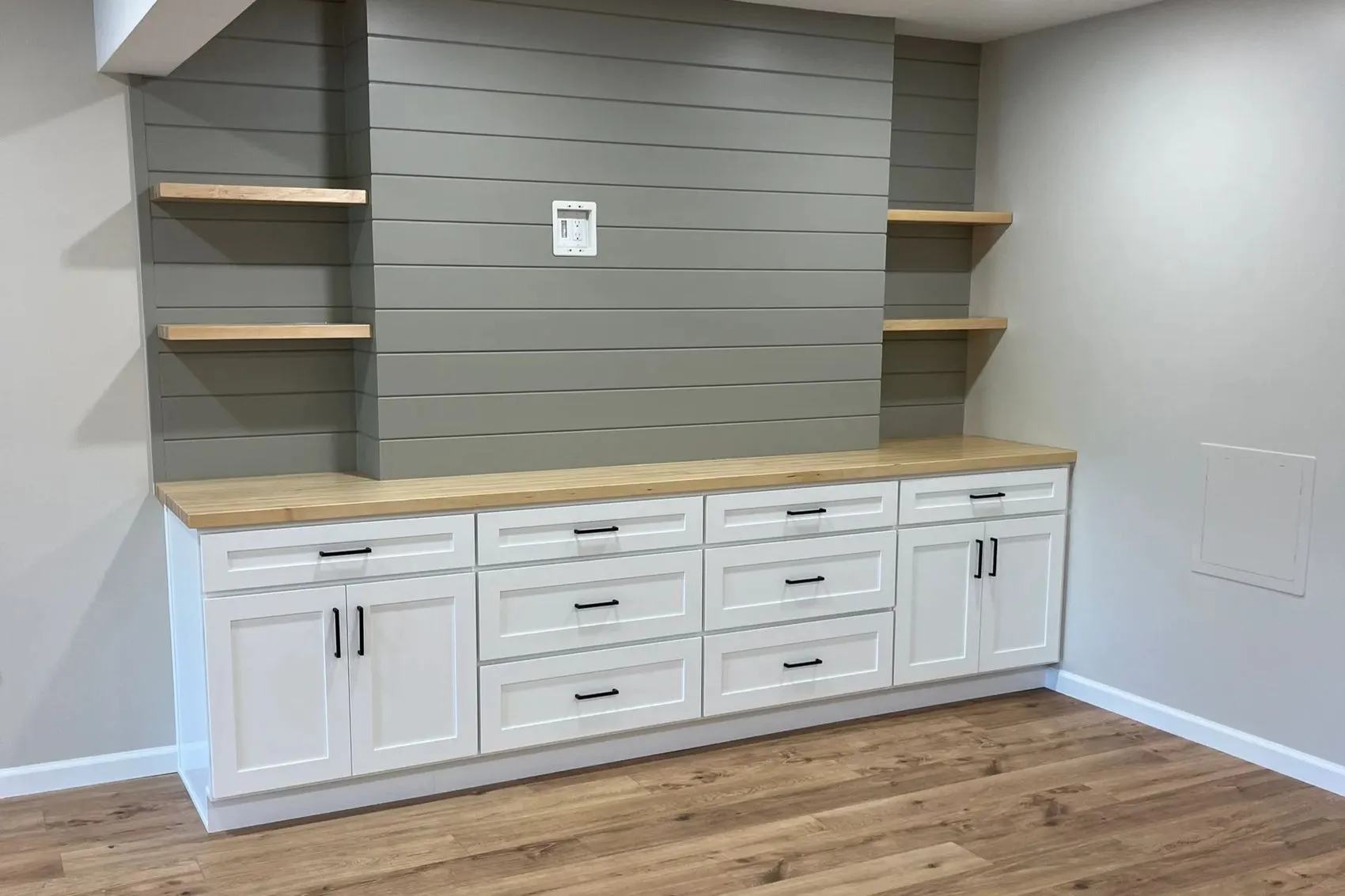 Modern built-in cabinet with white drawers and doors, wooden countertop, and wooden shelves on a gray paneled wall.
