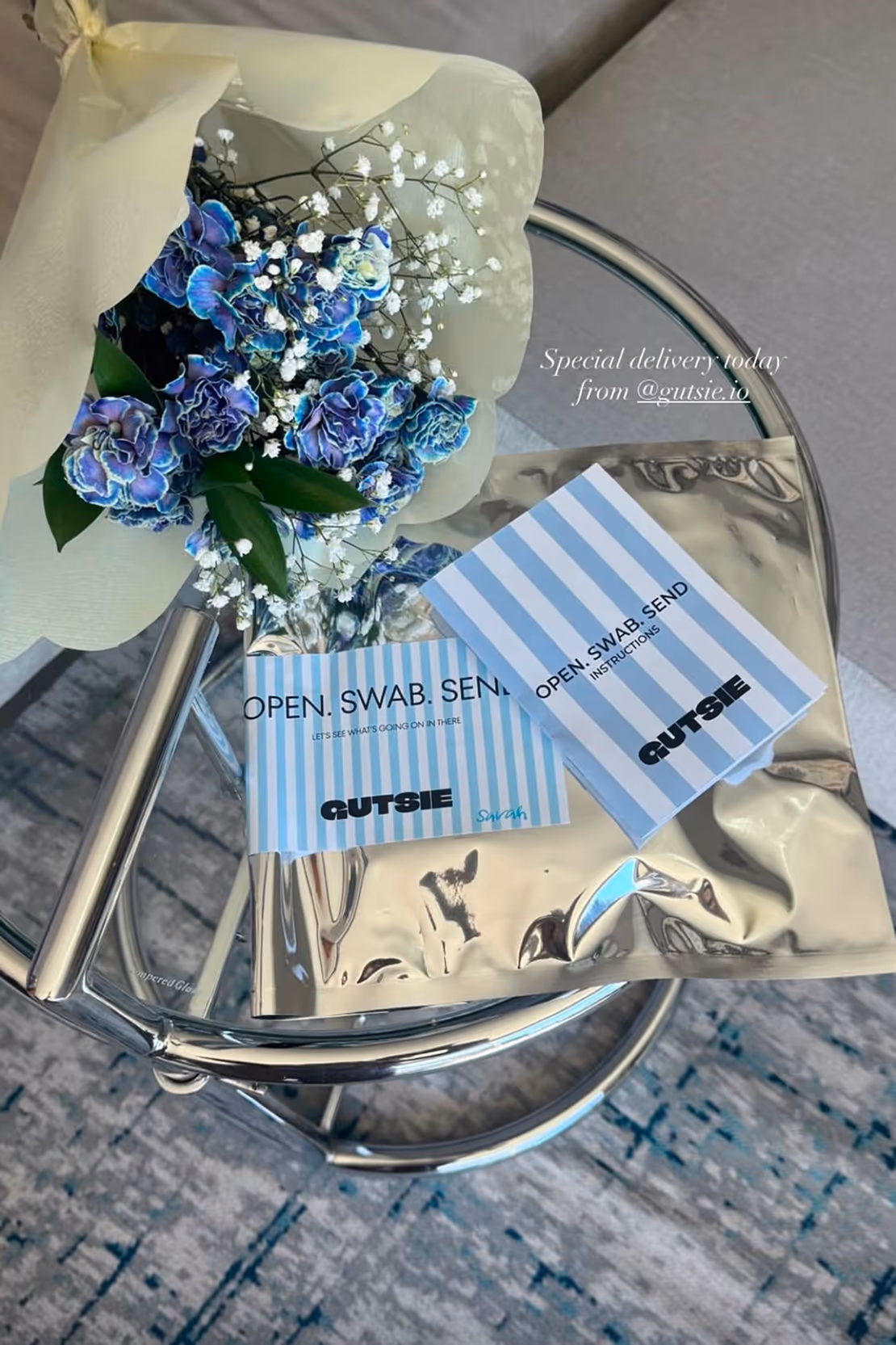 Blue and white bouquet with Gutsie branded COVID-19 test swab kit on a reflective round table.