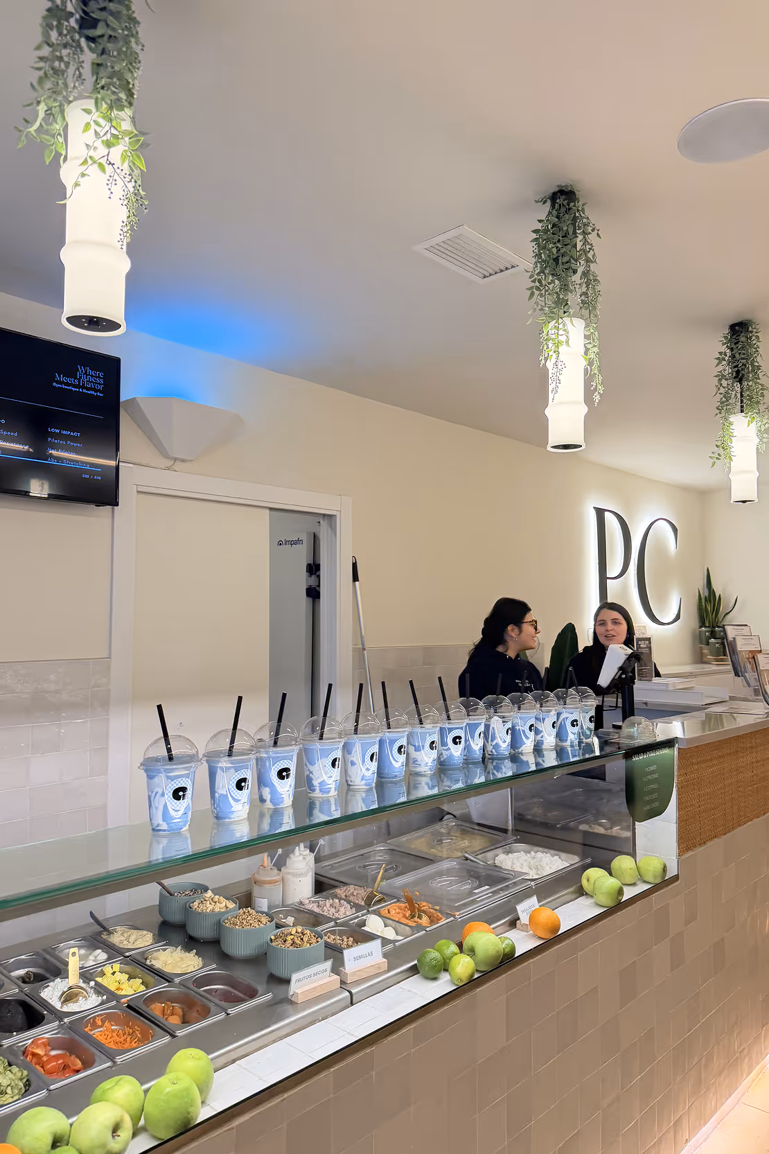 Counter at a juice or smoothie bar with multiple cups with straws lined up and two employees talking behind the counter.