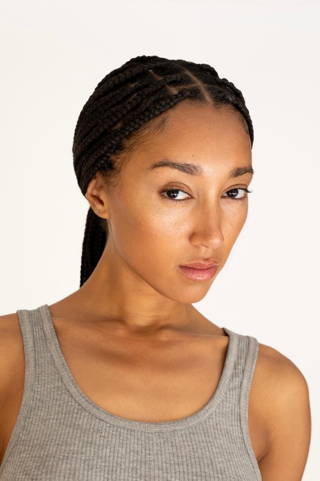 Portrait of a woman with braided hair wearing a gray sleeveless top, looking confidently at the camera.