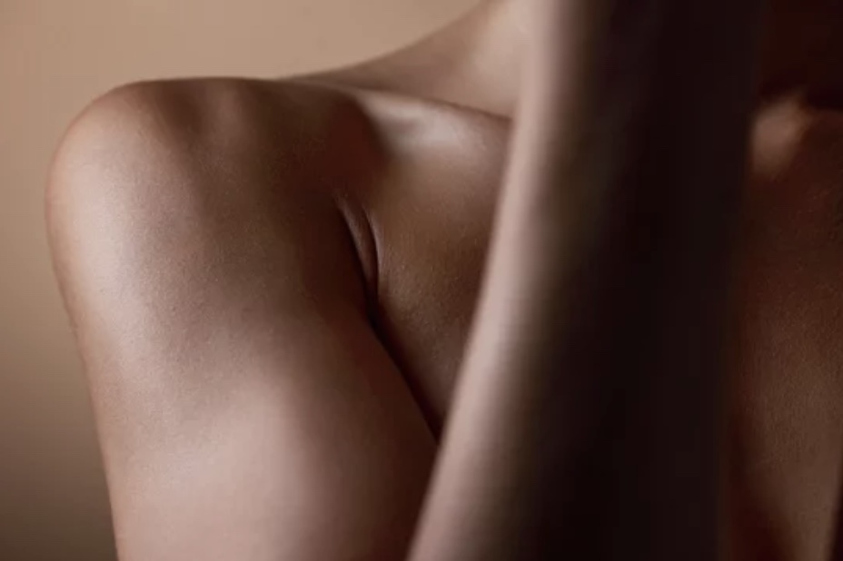 Close-up of a bare shoulder and upper arm with smooth skin against a soft brown background.