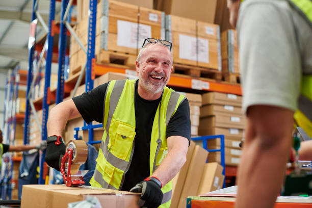 Smiling warehouse worker in a high-visibility vest sealing a cardboard box