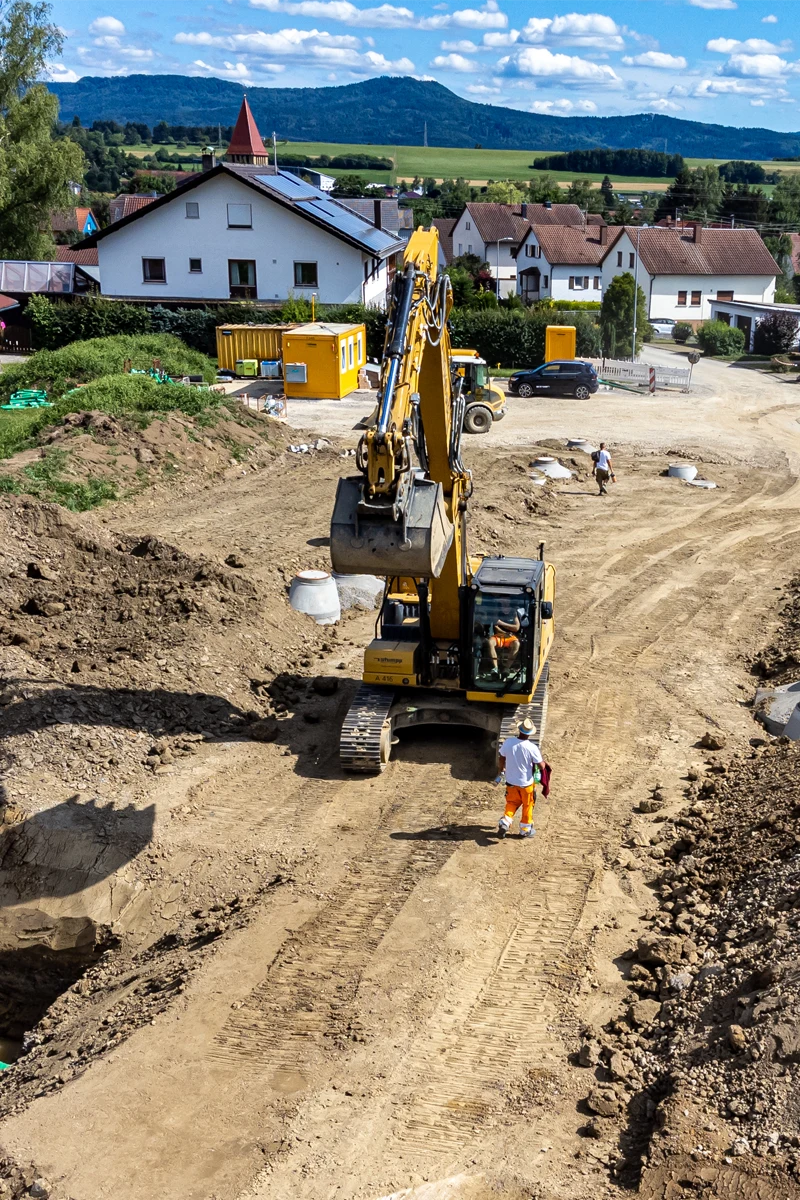 Bagger bei Erschließungsarbeiten in Grosselfingen, Baugrube mit Arbeitern und angrenzender Wohnbebauung.