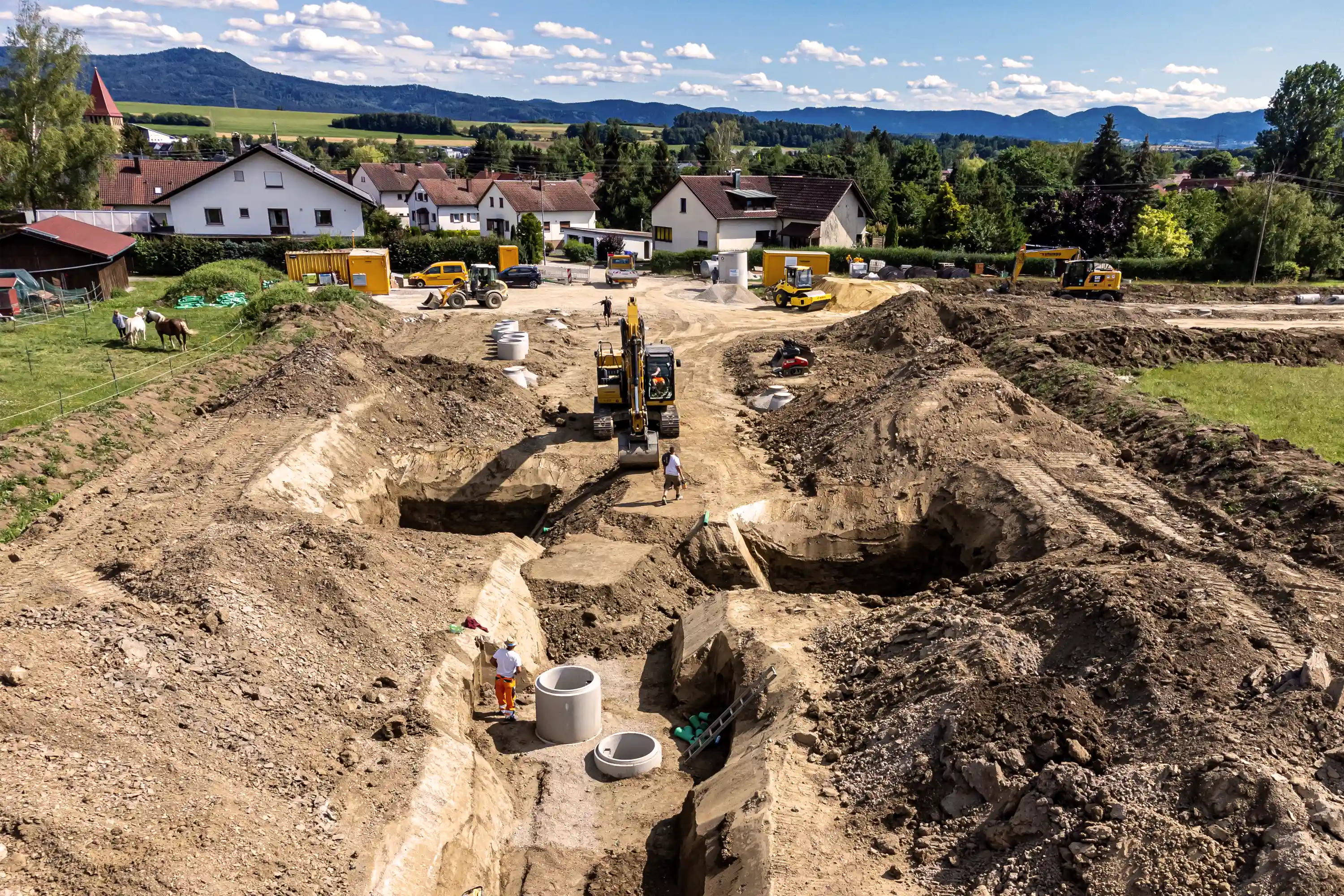 Baugebiet in Grosselfingen mit Erdarbeiten, Baggern und verlegten Betonringen für die Infrastruktur.