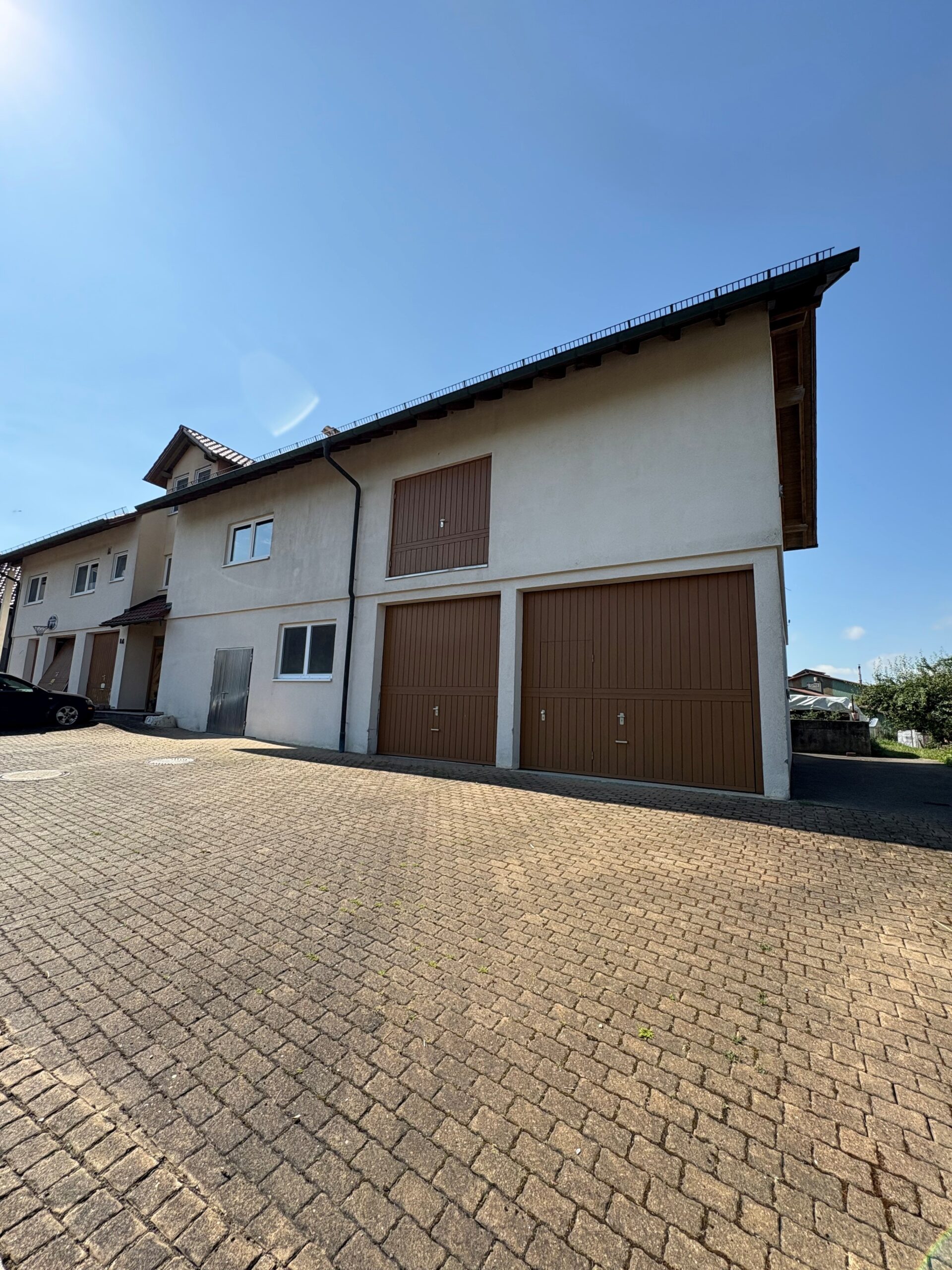 Großes Wirtschaftsgebäude mit zwei braunen Garagentoren und gepflastertem Hof unter klarem blauem Himmel
