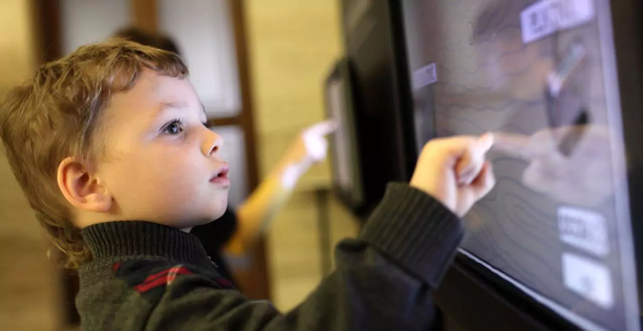 Young child using a touchscreen display, pointing at the screen with focused expression.