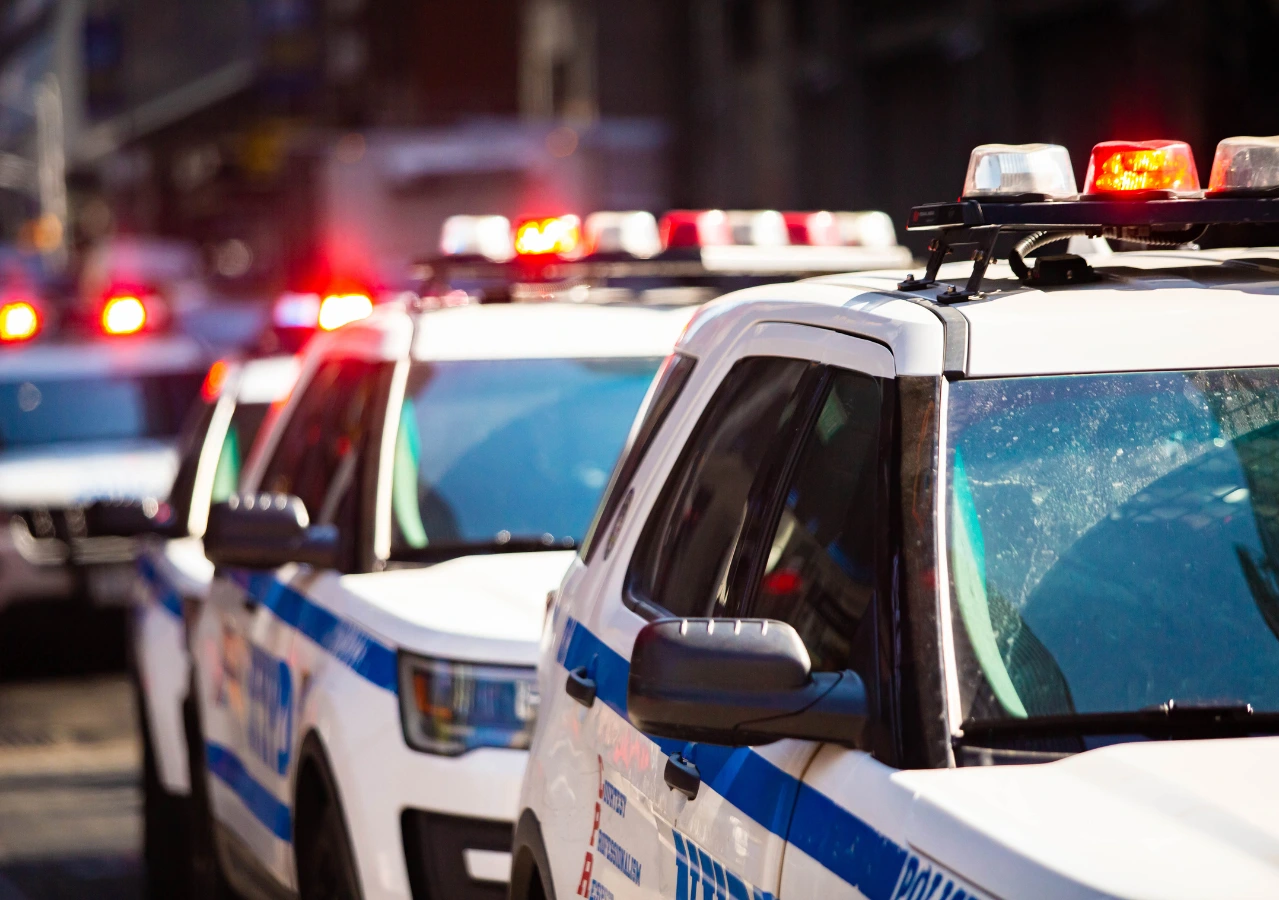 A line of white police SUVs with flashing red and blue lights parked on a city street.