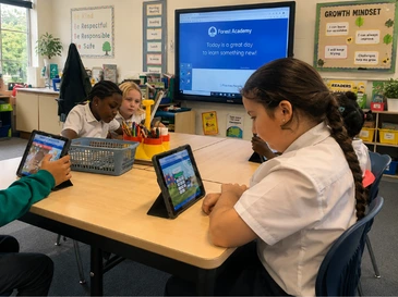 Students in school uniforms sitting around a table, using tablets in a classroom.