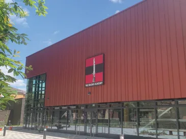 Modern red building with large windows and a sign reading The Soldier Academy under clear blue sky.