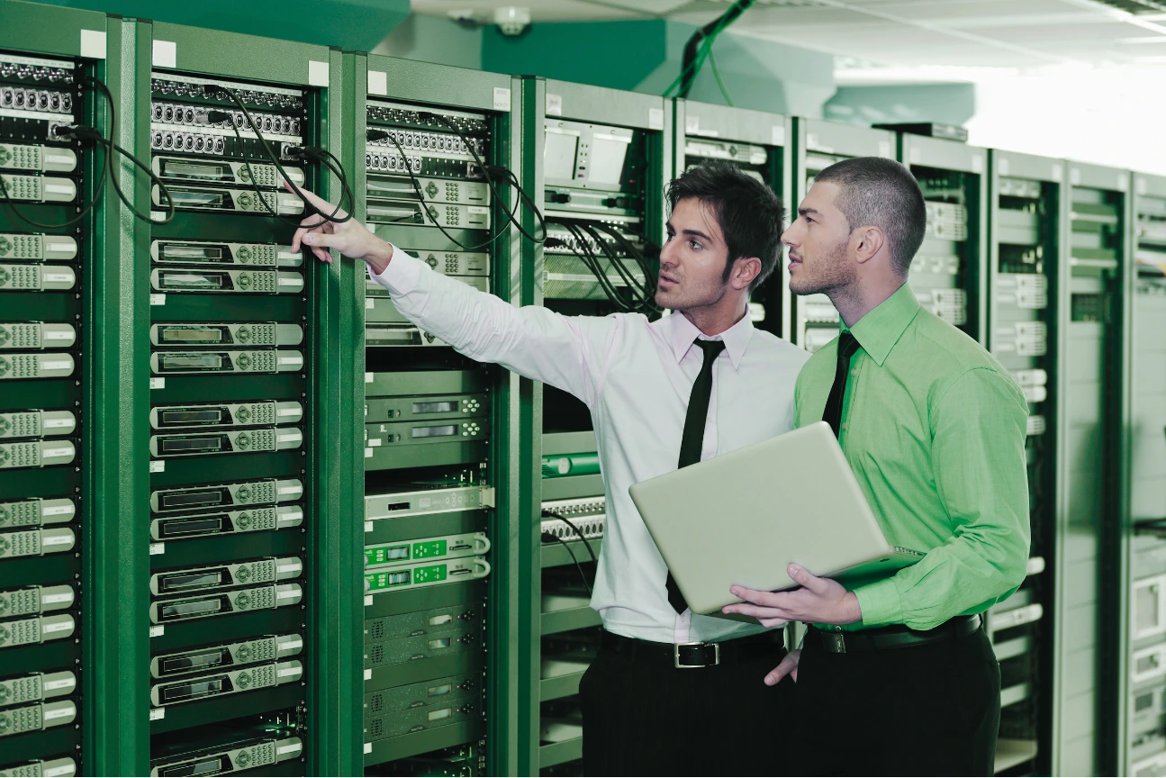 Two IT professionals inspecting and discussing servers in a data center rack, one holding a laptop.