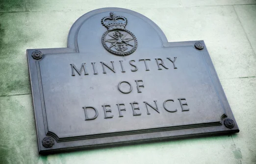 Plaque on a stone wall reading 'Ministry of Defence' with a military emblem and crown above.