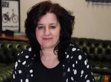 Latifa Hamdan, wearing a black shirt with white polka dots sitting on a green leather couch.