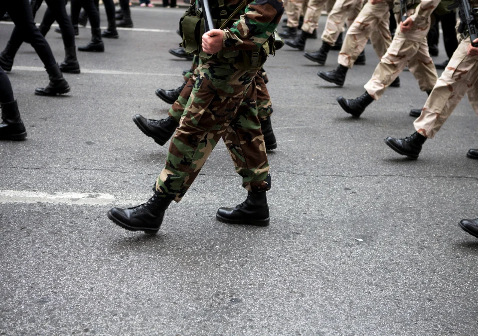 Soldiers in camouflage and tan uniforms marching on an asphalt road.