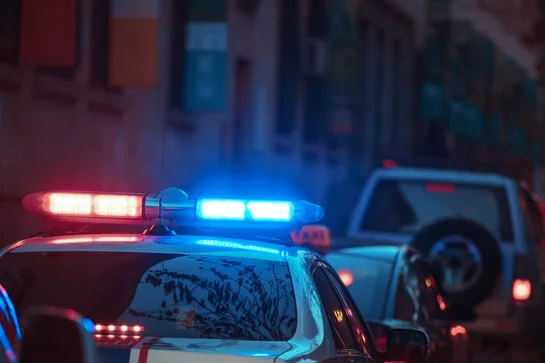 Police car with red and blue flashing lights on a city street at dusk.