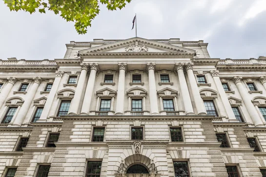 White neoclassical government building with columns and a flag on top under cloudy sky.