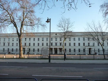 Wide front view of a large white neoclassical building with many windows and a black iron fence.