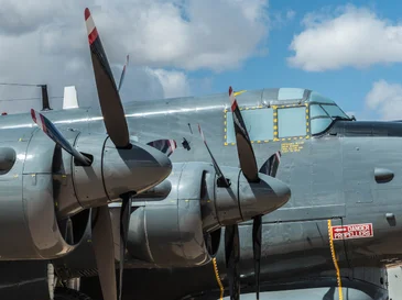 Close-up of a silver vintage propeller aircraft with three blades under a partly cloudy sky.