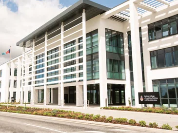 Modern multi-story building with large glass windows and white pillars under a partly cloudy sky.