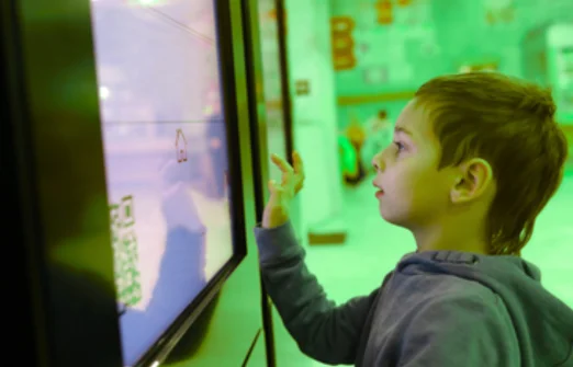 Young boy using an interactive touchscreen exhibit indoors with a green-lit background.
