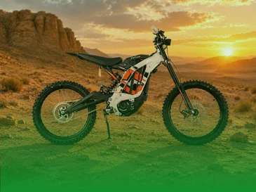 Electric dirt bike parked on rocky desert terrain with sun setting behind mountains.