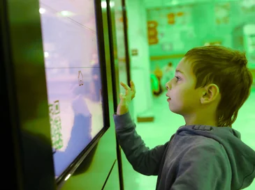 Young boy using an interactive touchscreen display in a brightly lit indoor space.