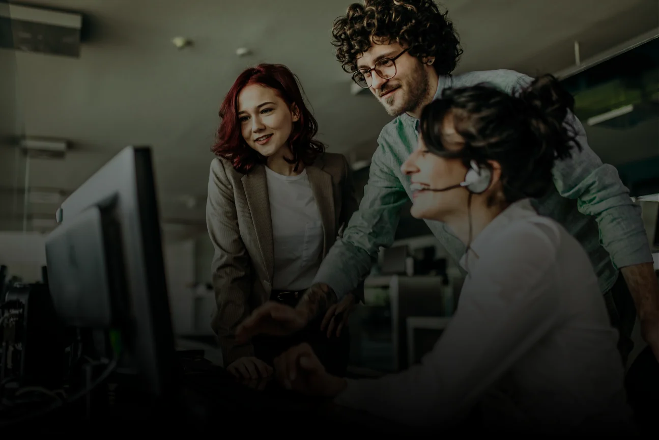 Three coworkers smiling and looking at a computer screen in a modern office.