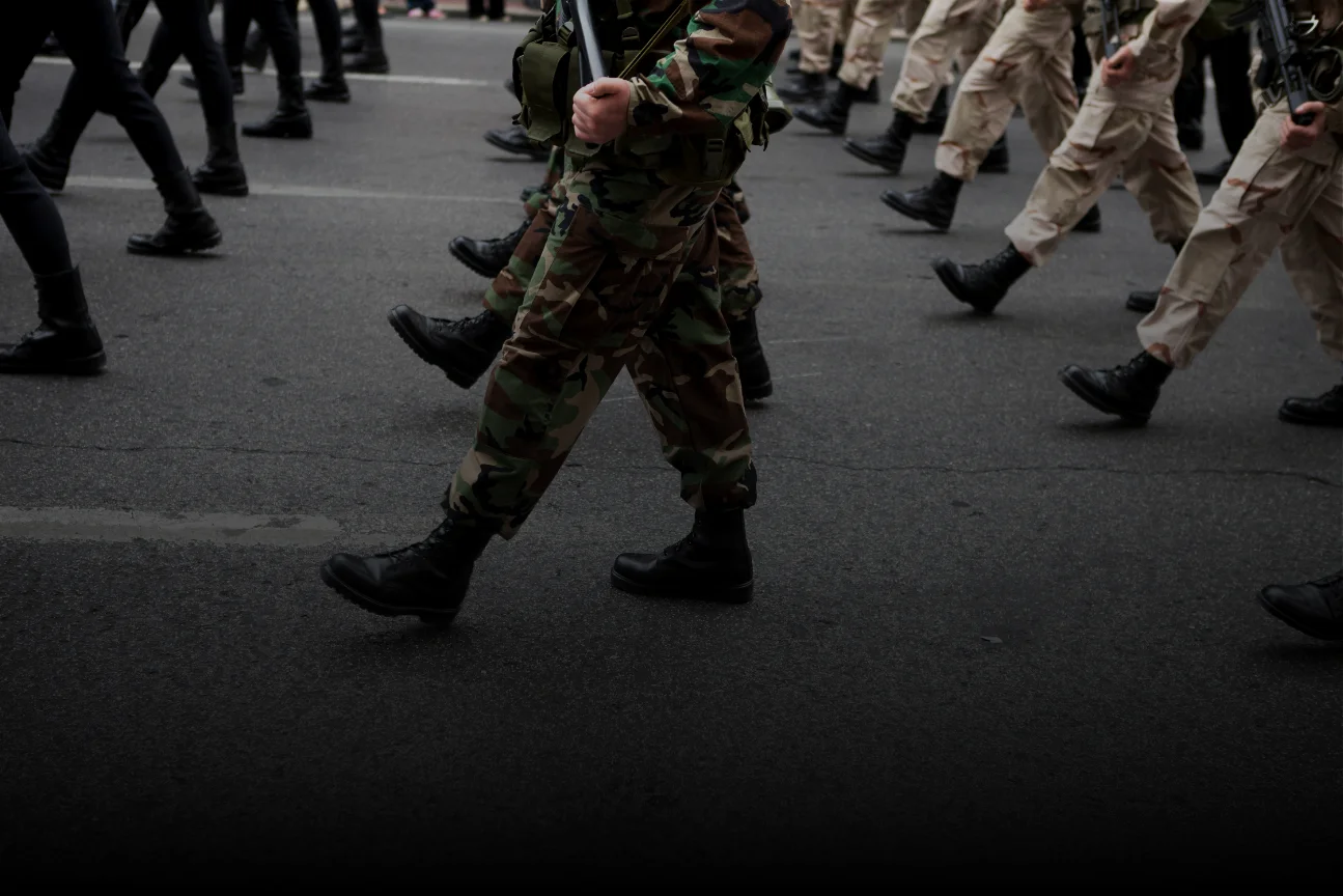 Military personnel marching in formation wearing different camouflage and beige uniforms with black boots.