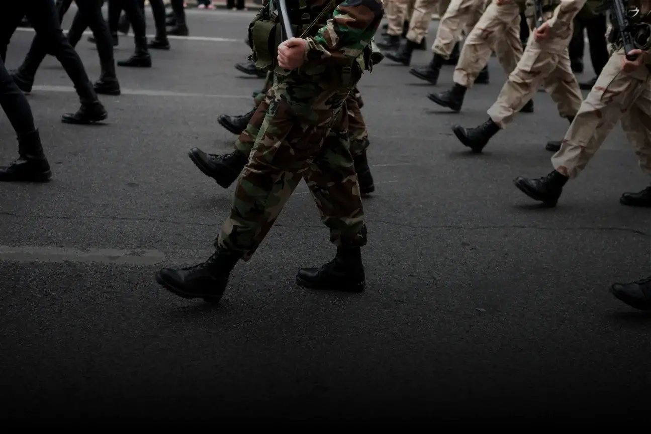 Military personnel marching in formation wearing different camouflage and beige uniforms with black boots.