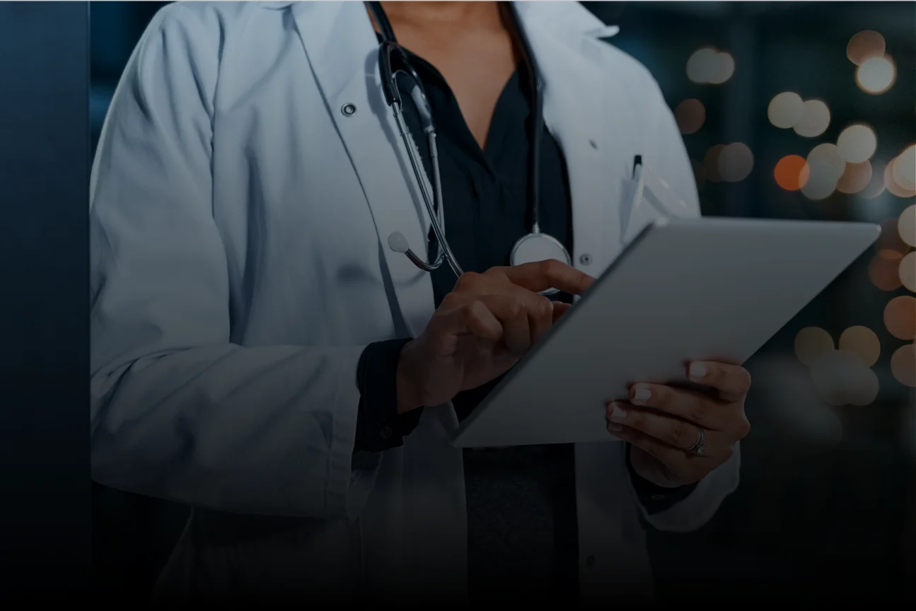 Medical professional in white coat using a tablet with stethoscope around their neck.
