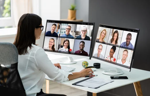 Woman participating in a video conference on two monitors showing colleagues' faces.