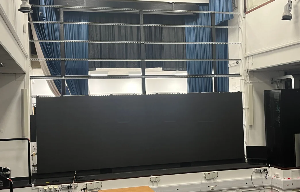 Large LED video wall mounted on a stage in a room with blue curtains and white walls.