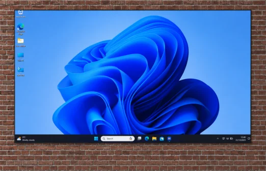 Large wall-mounted screen showing Windows 11 desktop with blue abstract wallpaper on brick wall.