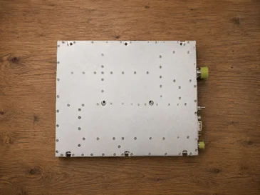 A metal electronic component with perforations and two yellow connectors on a wooden surface.