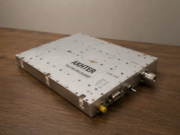 Metal rectangular electronic device labeled AKHTER with multiple connectors on a wooden surface.