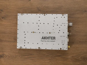 Metal electronic device labeled AKHTER Part No: AKLS0AMP on wooden surface with connectors on side