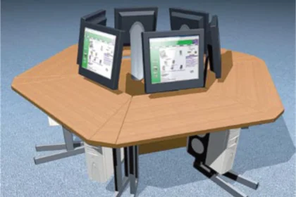 Hexagonal wooden table with six monitors facing inward, each paired with a computer tower below.