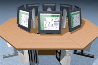 Octagonal wooden desk with eight computer monitors arranged for individual users around it.