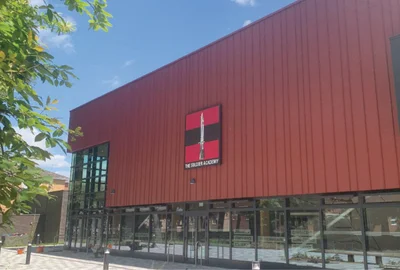 Red building with glass windows and a sign reading The Soldier Academy under a clear sky.