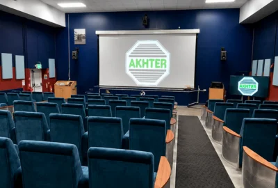 Empty small theater with blue seats facing a screen displaying the word AKHTER in green.