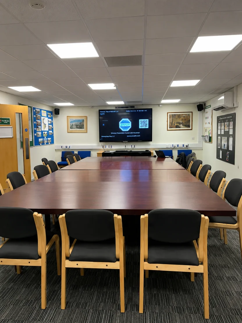 Empty conference room with long wooden table, chairs, wall-mounted TV displaying a welcome screen.