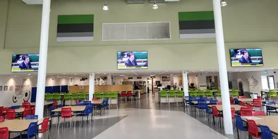 Wide room with colorful chairs and tables, three TVs on wall showing same content.