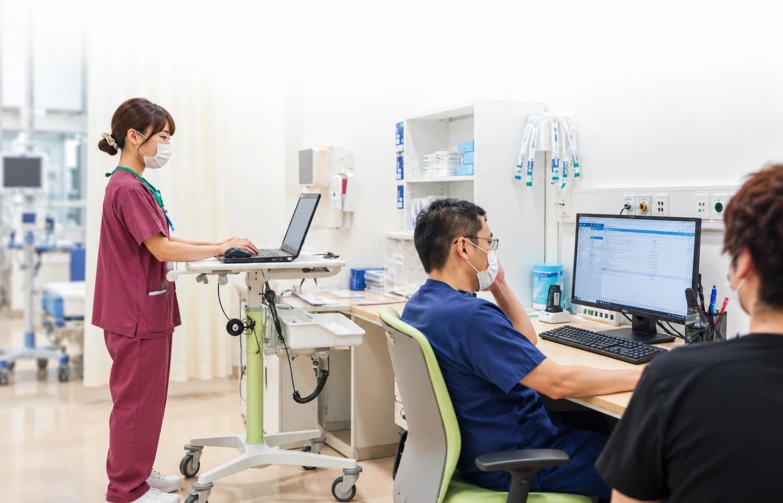 Healthcare staff using a laptop and desktop computer in a bright clinical workspace, illustrating hospital computing and IT solutions.