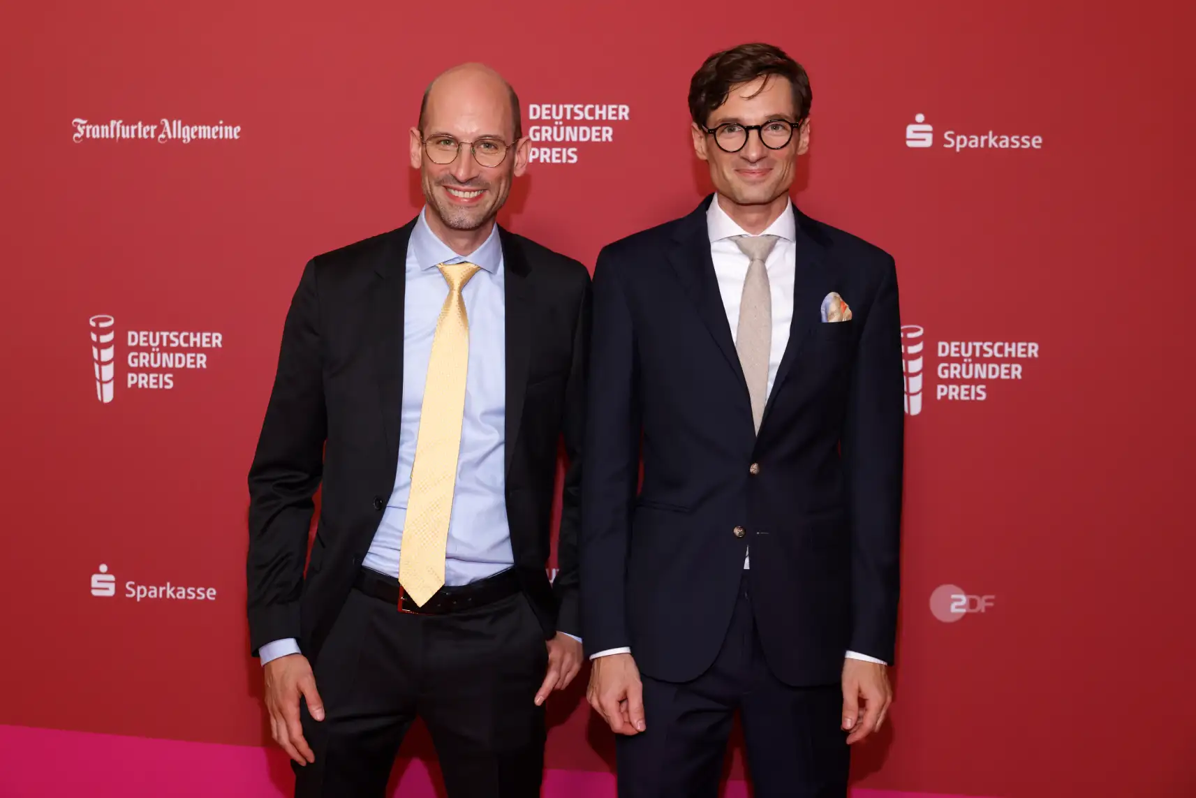 Two men in suits and glasses standing side by side in front of a red backdrop with Deutscher Gründerpreis, Frankfurter Allgemeine, Sparkasse, and ZDF logos.