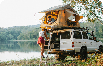 Smiling woman and child with red hair hugging on a sandy beach near an orange boat with a mountain in the background.